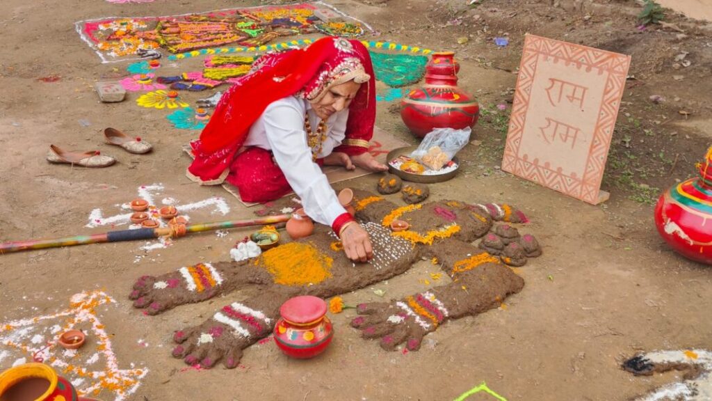 A woman in traditional Haryanvi attire performing Gordhan Pooja by decorating cow dung with flowers and colours in a village courtyard