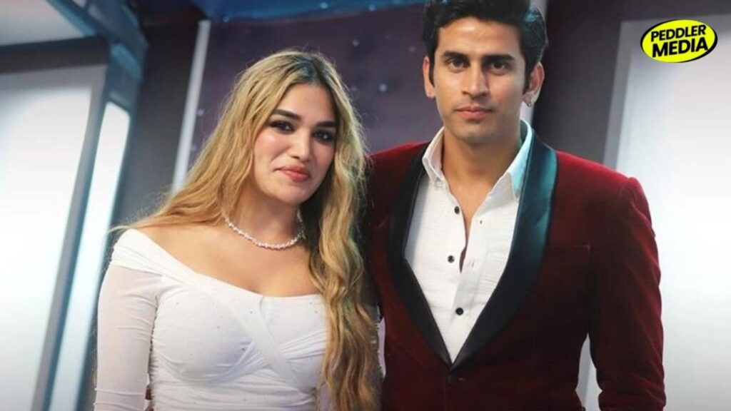 Gullu and Kaira, contestants from MTV Splitsvilla 16, pose together during the reality show in a glamorous indoor setting. Kaira wears an off-shoulder white dress while Gullu appears in a maroon velvet blazer and white shirt.