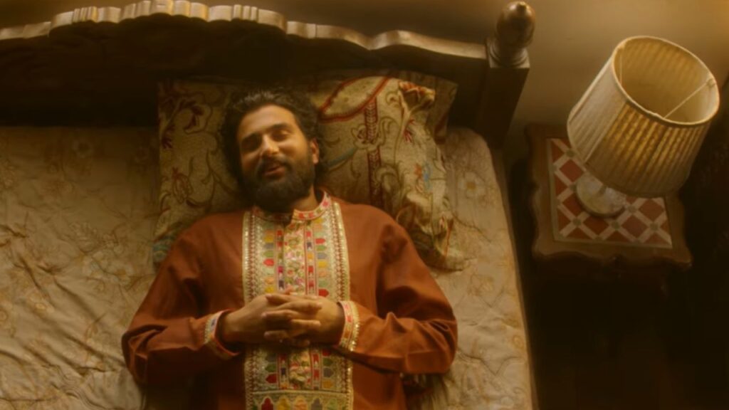 MC Square lying on a traditional wooden bed in a dimly lit room during “Long Way from Home,” capturing the loneliness and emotional weight of remembering a fading past.