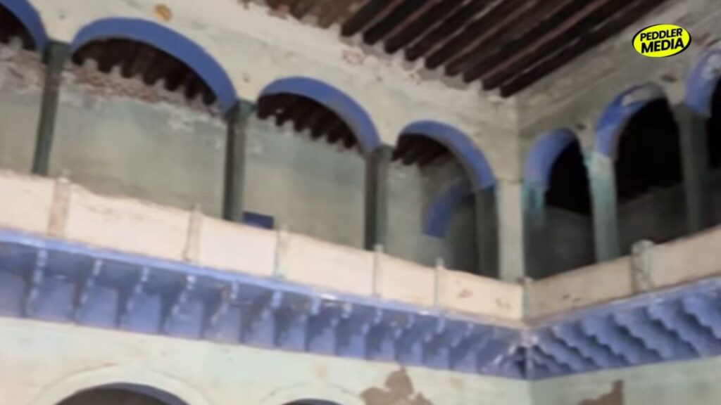 Interior view of an old Haryana Chaupal courtyard with blue arches and deteriorating wooden roof