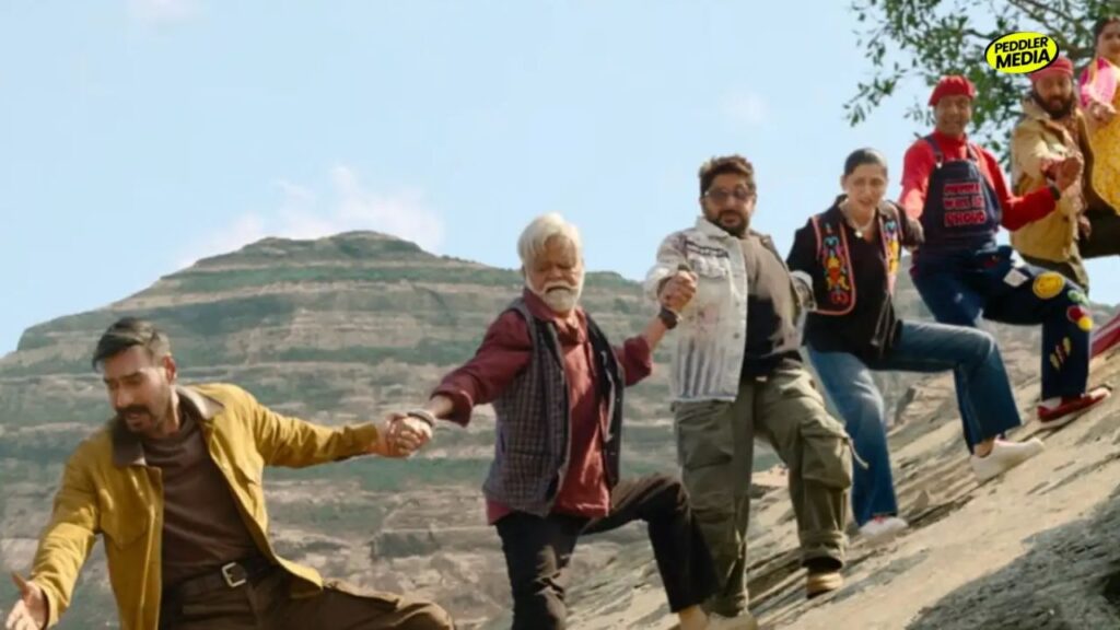 Dhamaal 4 cliff hanging scene featuring Ajay Devgn, Arshad Warsi and cast members holding hands.