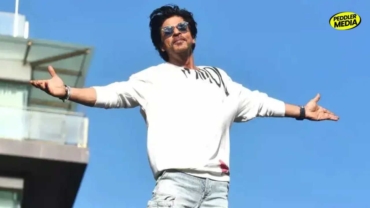 Shah Rukh Khan posing with his arms open against a blue sky