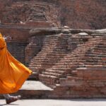 Buddhist monk walking beside ancient brick stupa ruins