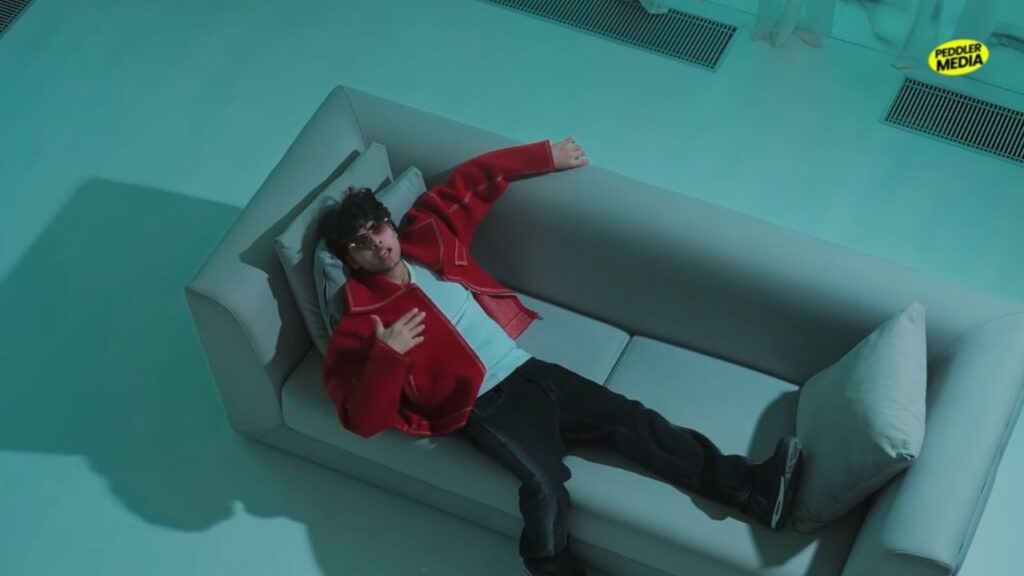 Krish Rao Wake Up Haryanvi song music video still showing the artist in a red jacket resting on a grey couch.
