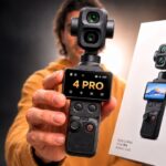 A person holding the new DJI Osmo Pocket 4 Pro camera next to its retail Vlog Combo box, showcasing the best tools for vlogging in 2026.