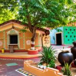 A colourful traditional village courtyard showing mud houses and clay pots representing the heritage style of Mhari Mati Agro Tourism Hisar.