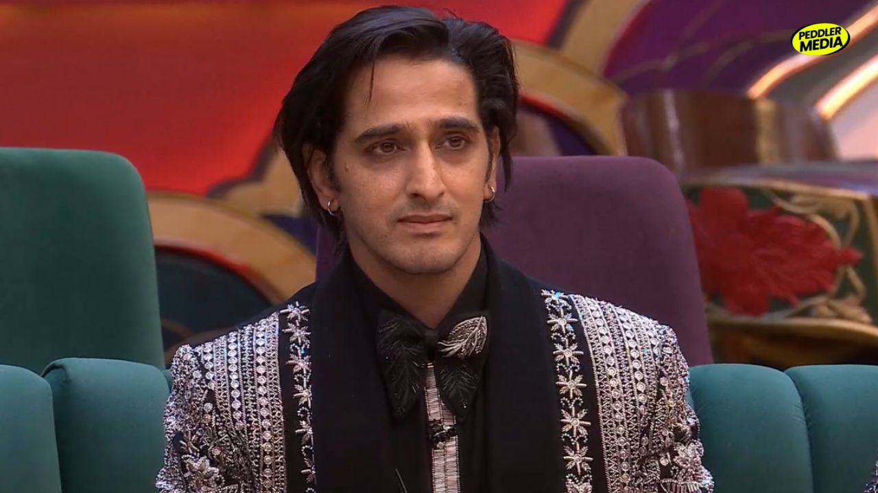Qazi Touqeer looking front while sitting on a sofa inside the Bigg Boss house.